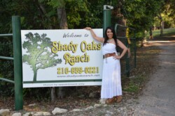 Woman standing in front of welcome to shady oaks sign